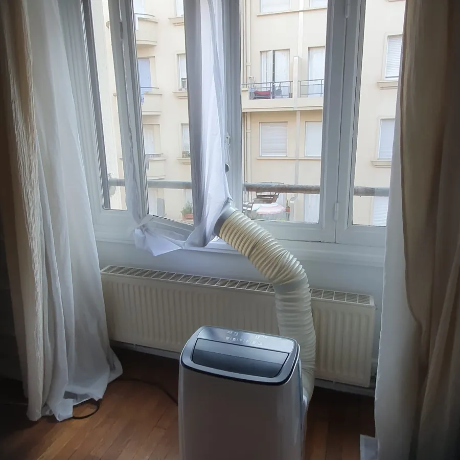 Climatiseur mobile installé dans le salon d'un appartement à Lyon, tuyau d'évacuation raccordé à la fenêtre avec kit de calfeutrage